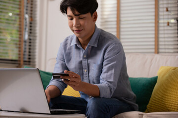 Asian man makes a payment via the internet. On the sofa at home, a shopper shops online using a credit card and a smartphone. The concept of internet shopping.