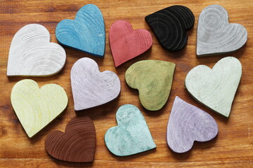 Multicolored hearts on a wooden background. Many wooden painted hearts in different colors. 