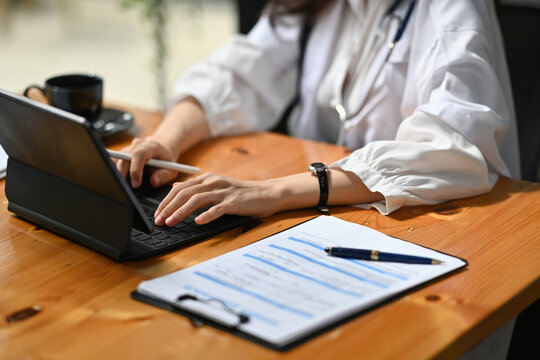 Cropped image of the doctor's hand using a digital tablet at the working desk surrounded by a prescription and coffee cup.