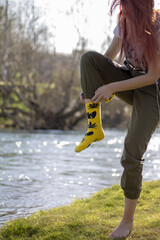 Vertical shot of a young female taking off the socks on the riverbank