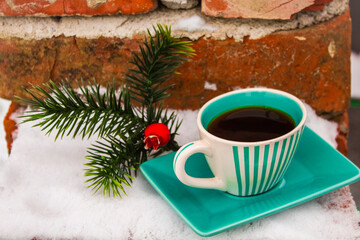 Green set cup with a saucer with black coffee near the Christmas tree artificial branch in the snow 