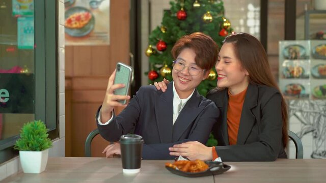 Young adult lesbian couple taking selfie with smartphone, LGBT Pride Month, Gay Pride Symbol. Happy lesbian couple taking picture on smartphone in coffee shop.
