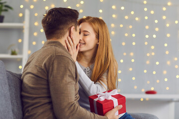 Fototapeta na wymiar Young happy couple in love kissing during giving presents and celebrating holiday at home with decorated interior background. Christmas, Valentines day, birthday, holiday, love, togetherness concept
