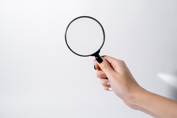 Female hand holding a magnifying glass with black frame on a white background