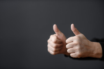 Two male hands give a thumbs up on a dark background. Close-up and copy space