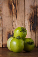 Green tomatoes on brown wooden kitchen rustic background. Farmer fresh organic product. Vegan eco-friendly no animal food. Copy space, vertical
