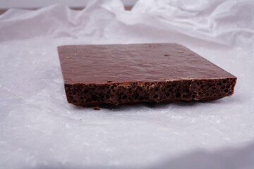 Porous chocolate bar on white paper. Bubbled or spongy chocolate, tasty sweets, carbohydrate food,...