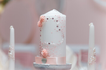 Beautiful white candle with pink decorative elements, roses and heart for just married wedding presidium or Valentines day decor for romantic dinner.