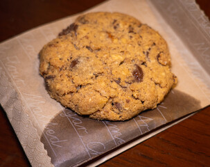 A big chocolate chip cookie placed on a butter paper packet. Wooden background. 