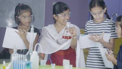 Teacher giving notes to students about Chemistry lab experiment by holding chemical flask - concept of science laboratory teaching, children education and learning