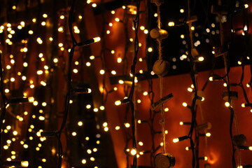 Fototapeta na wymiar Warm red Christmas background with hanging fairy or string lights indoors and twine with wooden additions - cozy, warm winter wallpaper or screensaver 