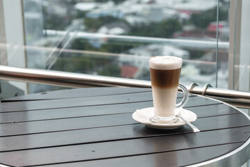 A glass of coffee latte on a table against a blurred background.