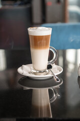 A glass of coffee latte on a table against a blurred background.