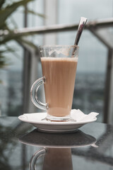 A glass of coffee latte on a table against a blurred background.