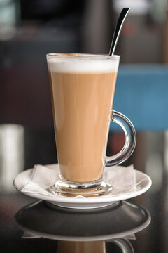 A glass of coffee latte on a table against a blurred background.