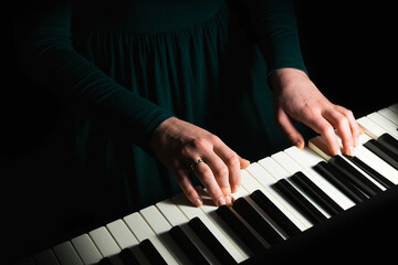 Female pianist in green dress plays chord on black piano with both hands. Touches gently the...