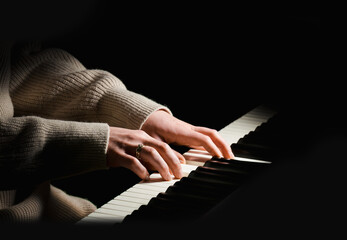Female pianist in sweater dress plays chord on black piano with both hands. Touches gently the keyboard. © irekpod