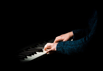 Female pianist in blue sweater plays chord on black piano with both hands. Touches gently the...