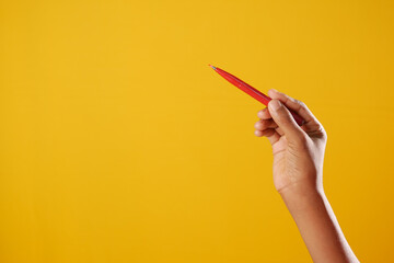 holding a red color pencils against yellow background 