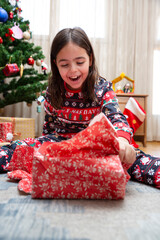 Very happy little Caucasian girl opening Christmas presents at home.