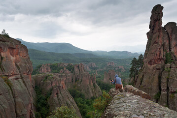 Photographer is taking a landscape photo sitting on red rock formations in Belogradchik, Bulgaria.