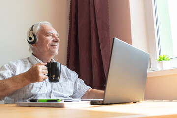senior old man male sit desk, home office notebook work distance freelancer listen music headphones happy call center