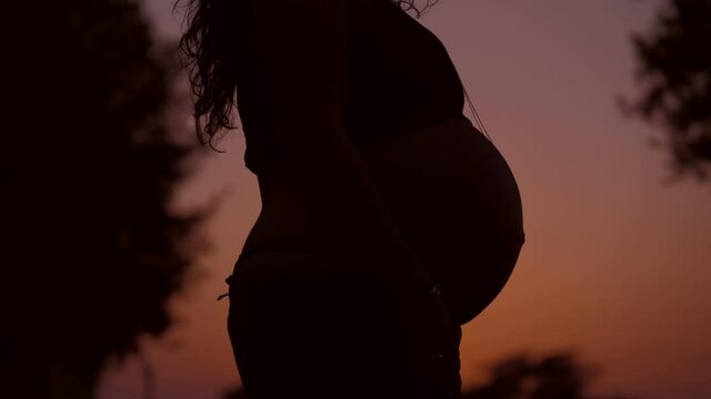 beautiful pregnant woman with uncovered belly in the sunset light