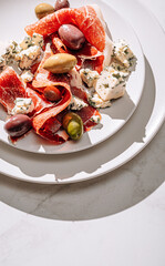 cool white wine in a glass near a plate with sliced jamon, dove cheese and various olives. a light snack on a hot day. classic italian food.