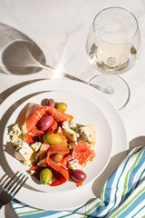 cool white wine in a glass near a plate with sliced ham, dove cheese and various olives
