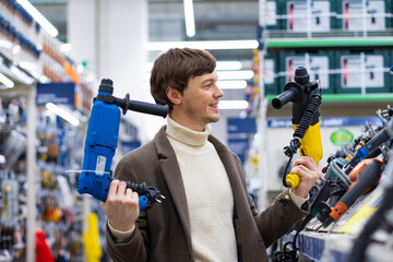 Young short-haired man with bristle in woolen sweater and brown coat chooses between pulverizers...