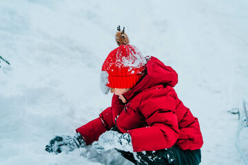 Fototapeta na wymiar A boy in a red jacket and a red hat plays in the snow