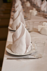 a white textile napkin stands beautifully on a plate. set table for guests at the party, white plates and silverware.
