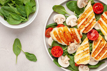 Vegetarian salad with spinach leaves, cherry tomatoes, mushrooms and grilled halumi cheese in a plate on the table. Top View