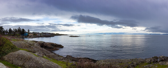 Panoramic View of Rocky Shore on the West Pacific Ocean Coast during cloudy winter evening. Taken at Saxe Point Park, Victoria, Vancouver Island, British Columbia, Canada.