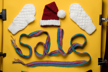 Word SALE is made with a knitted scarf, above it is a Santa Claus hat and mittens. Concept of New Year discounts and shopping. 