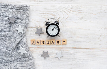alarm clock, sweater, decorative stars and letter "january"  on white wooden background. january month calendar concept. winter season. flat lay. copy space