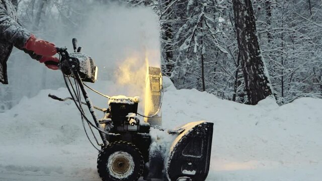 Snow-covered man cleans the road in winter with blower, snow removal equipment