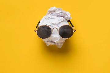 Crumpled white paper and sunglasses on it look like a face against a yellow background. Creative...