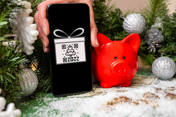 A hand holding a smartphone with a gift symbol and a QR code, a red piggy bank on gold coins...
