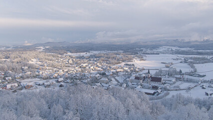 AERIAL: Winter morning sunbeams illuminate snowy valley and suburban village.