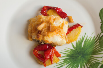 Plating of white fish varnished with toasted egg accompanied with red peppers, potatoes, and garlic on a plate with abstract decoration. Fish and healthy food.