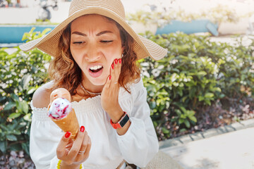 Traveler woman took a bite of cold and sweet ice cream and felt a sharp pain in her teeth due to...