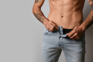 Sexy young man taking off his jeans on grey background