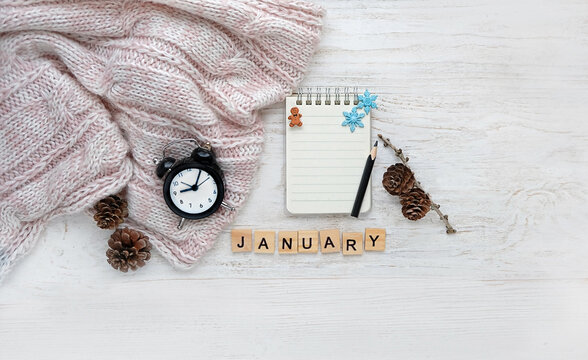 alarm clock, sweater, letter "january",  notepad, pencil, pine cones on white wooden background. january month calendar concept. winter season. flat lay. copy space