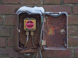 Dangerous Electrical Engineering: old electrical equipment with broken insulation on a brick wall outdoors.