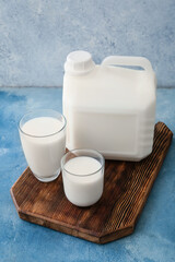 Gallon bottle and glasses of milk on color background