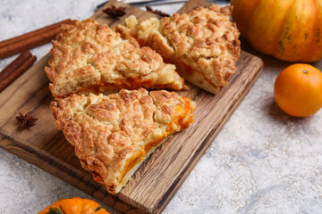 Wooden board with pieces of tasty pumpkin pie on grey background