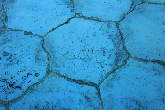 Turquoise blue bottom of a fountain full of water photographed during the daytime on a sunny day. Hexagon shaped tiles in a closeup.