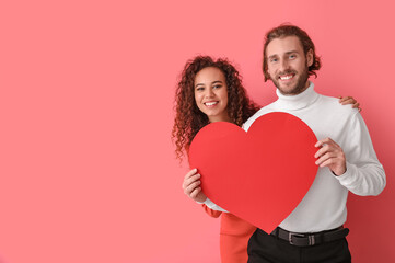 Happy young couple with red paper heart on color background. Valentine's Day celebration