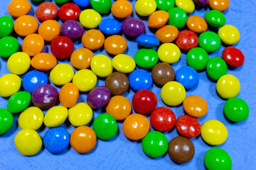 Fototapeta na wymiar Scattered colored candies on a blue background. Lots of colored sweets on a blue surface